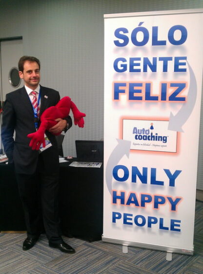 Pedro Amador de pie junto a un banner de Auto-coaching con un muñeco rojo